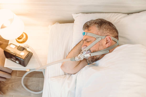 Sleeping man with chronic breathing issues considers using CPAP machine in bed. Healthcare, Obstructive sleep apnea therapy, CPAP, snoring concept