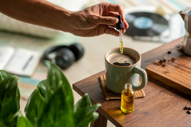 Man dropping CBD oil or Cannabis oil into a coffee cup while relaxing at home