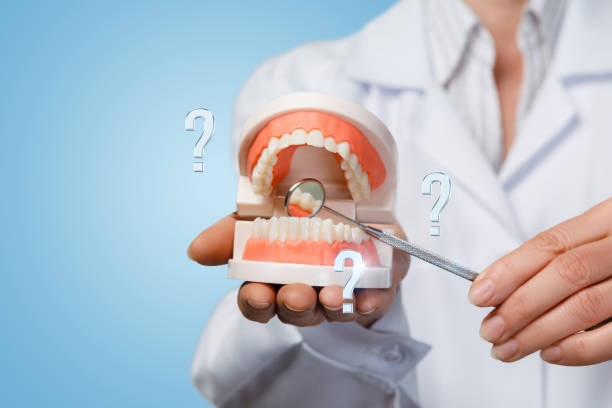 A closeup of doctor holding opened denture model with question marks around and pointing at teeth with dentist mirror. The concept of proper and innovative diagnostics and treatment.