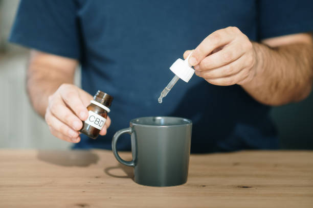 How to Use CBD Oil? - A person pouring CBD oil drops from a pipette dropper bottle into a cup