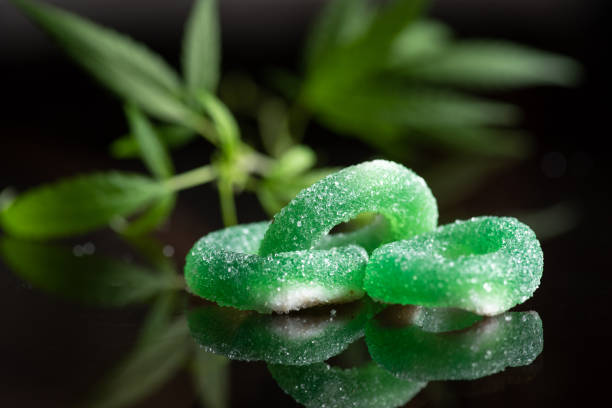 Colored gum candy jelly with marijuana leaves, on a black glass background. Sweet gummy candy with CBD, THC oil.