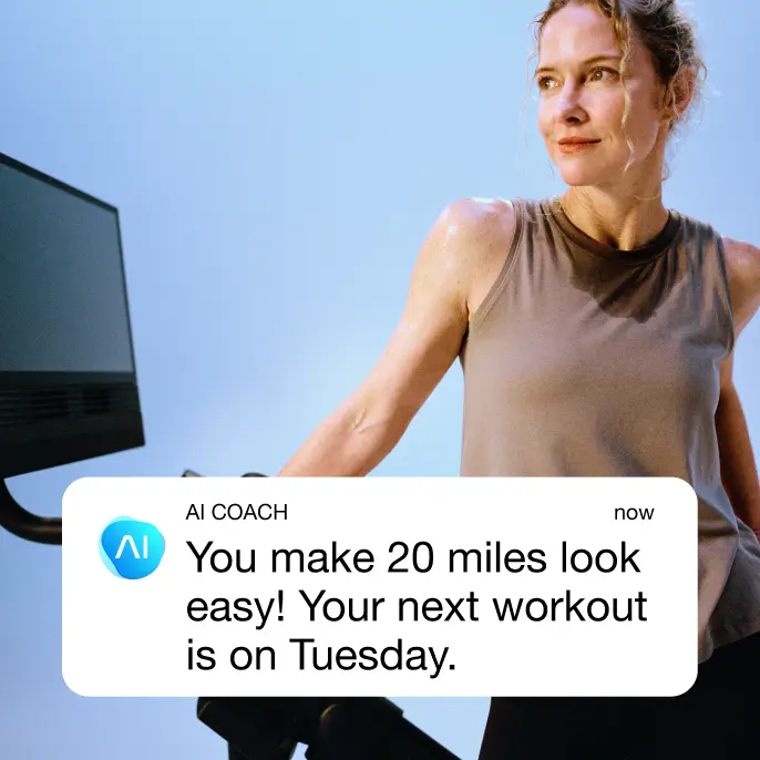 A woman leaning on a NordicTrack Bike with a screen with a message from the AI Coach saying "You make 20 miles look easy! Your next workout is on Tuesday.