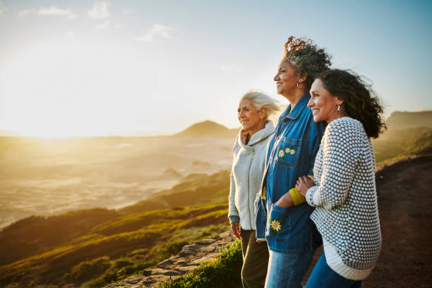 Carefree group of smiling mature female friends standing arm in arm together and looking out at the scenic coastal view during a road trip